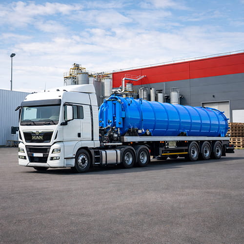 Naczepa asenizacyjna na ciężarówce MAN przed zakładem przemysłowym.